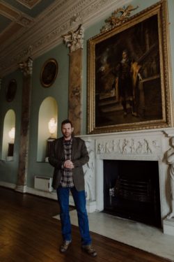 The 19th Earl of Devon standing next to a fireplace in Powderham castle