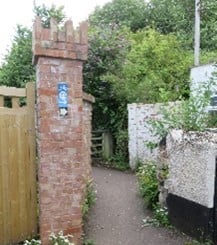 A path with a brick pillar on the left and a white wall on the right