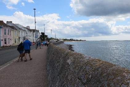 A stone wall with the sea on the right and a pavement on the left. 