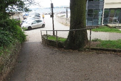 A path sloping downhill with a handrail and a tree on the right side.