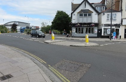 A pub on the other side of the road and a pedestrian central reservation with yellow bollards.