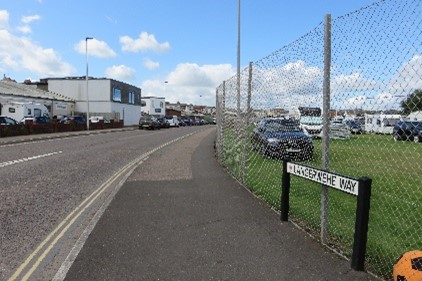 A tall metal chain link fence between a pavement and a grassy area.