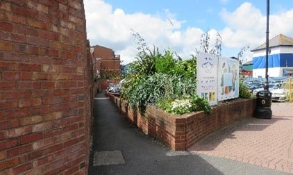 A brick wall by a pavement and a planted raised area.