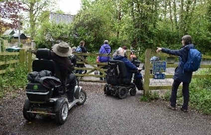 People using disability scooters going through a wooden gate.