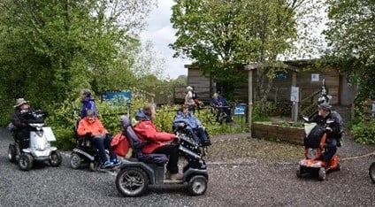 People using disability scooters on a path with trees in the background.