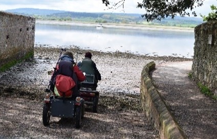 People using disability scooters on a slipway onto a beach.