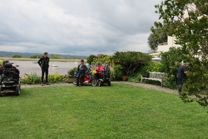 People using a lawn area with a bench and trees.