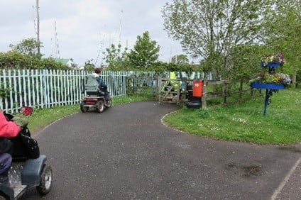 People using disability scooters on a path by a metal fence.