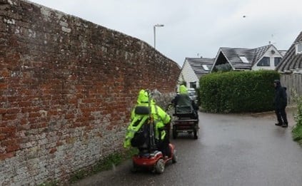 People using mobility scooters next to a high brick wall.