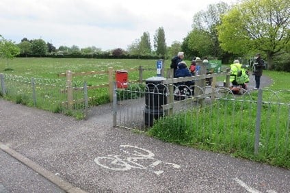 A cycle path with a gateway to a park area. People on mobility scooters are using the path.